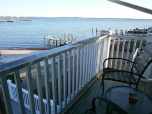 A balcony with chairs and tables overlooking the water.