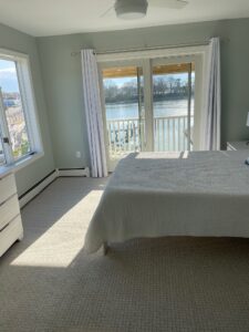 A bedroom with a bed, dresser and window overlooking the water.