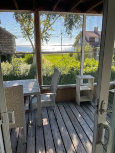 A porch with two chairs and table in front of the ocean.