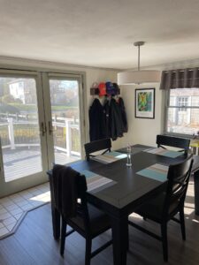 A dining room table with four chairs and two hanging coats.