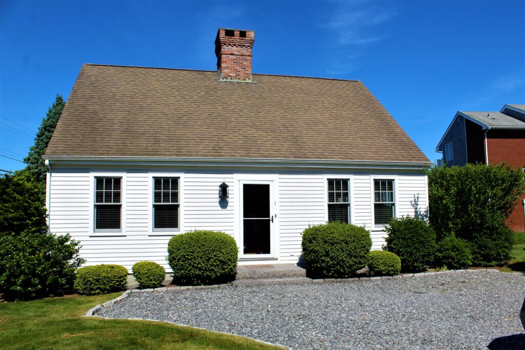 A white house with a brick chimney and bushes around it.